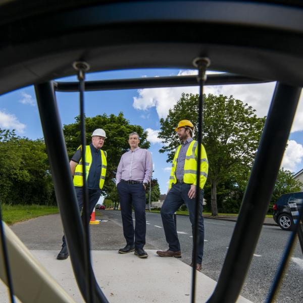 three men in construction PPE looking through bike spokes