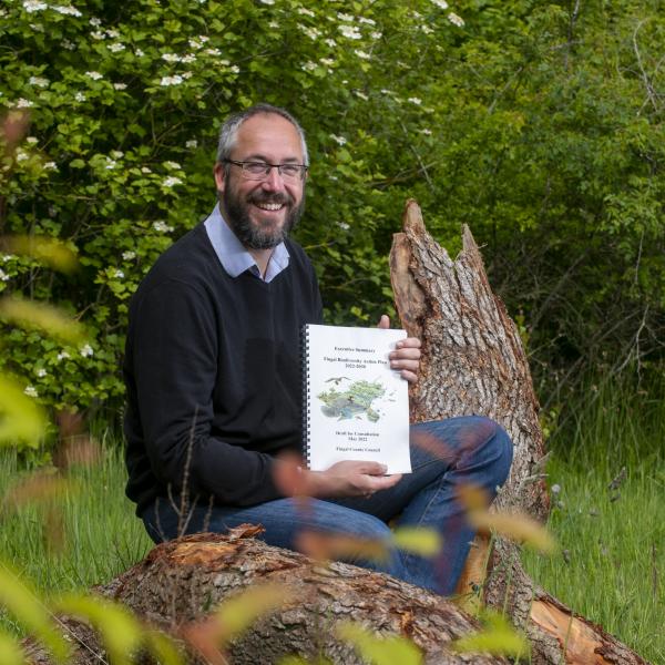 bearded man holding document while sitting on log in flowers and grass