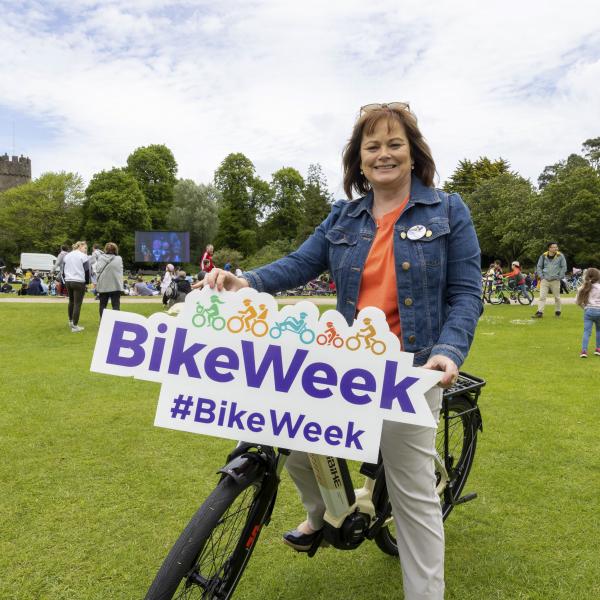 Woman on bike holding bike week promotional signage