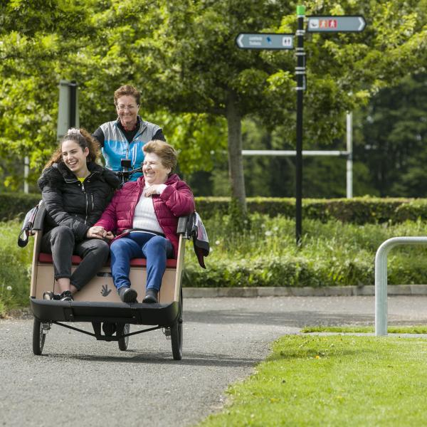 Two women being carried on cycling without age trishaw bike by volunteer