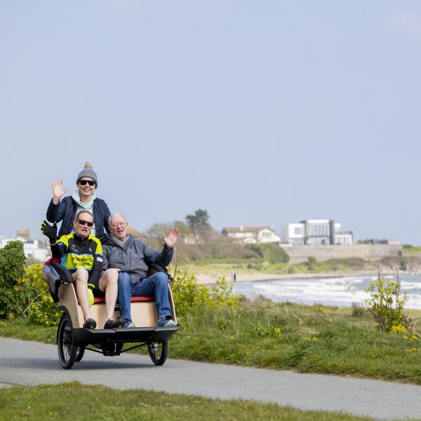 two men in trishaw seated with female cyclist to rear beach scene 