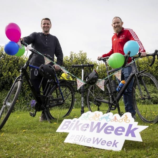 Two people standing with bikes and bike week sign