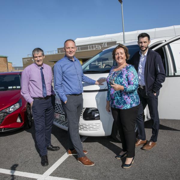 Woman holding keys stands next to vehicle surrounded by other people 