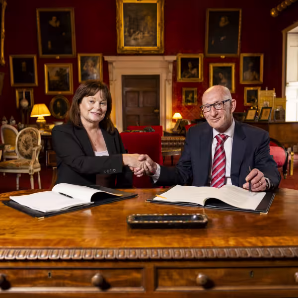 Man and woman shake hands over contract, seated at table