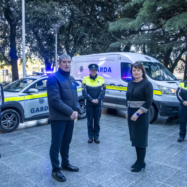 Sombre group of Gardai and staff standing in front of lit garda vehicles