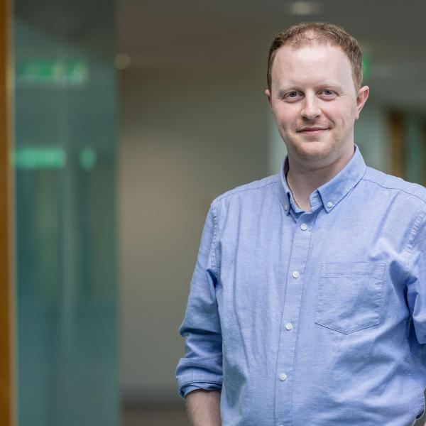 Man wit fair hair standing and smiling, wearing blue shirt.