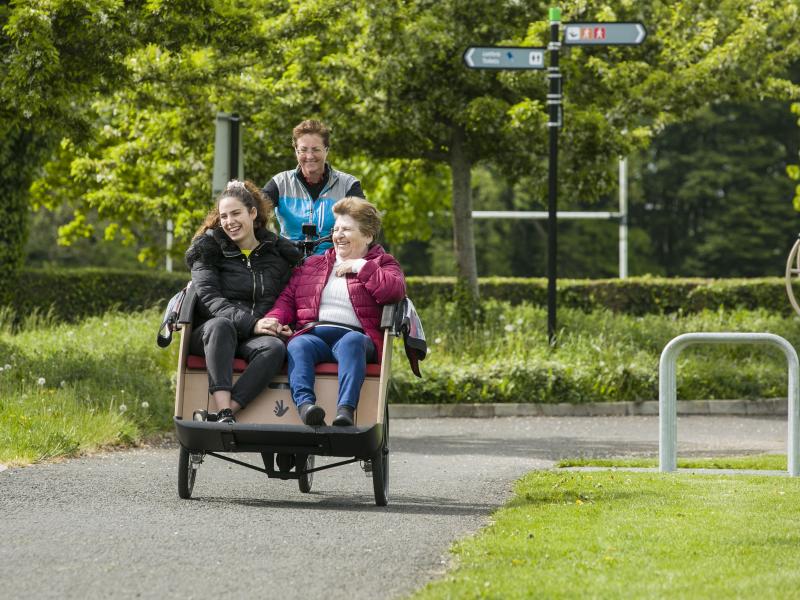 Two women being carried on cycling without age trishaw bike by volunteer