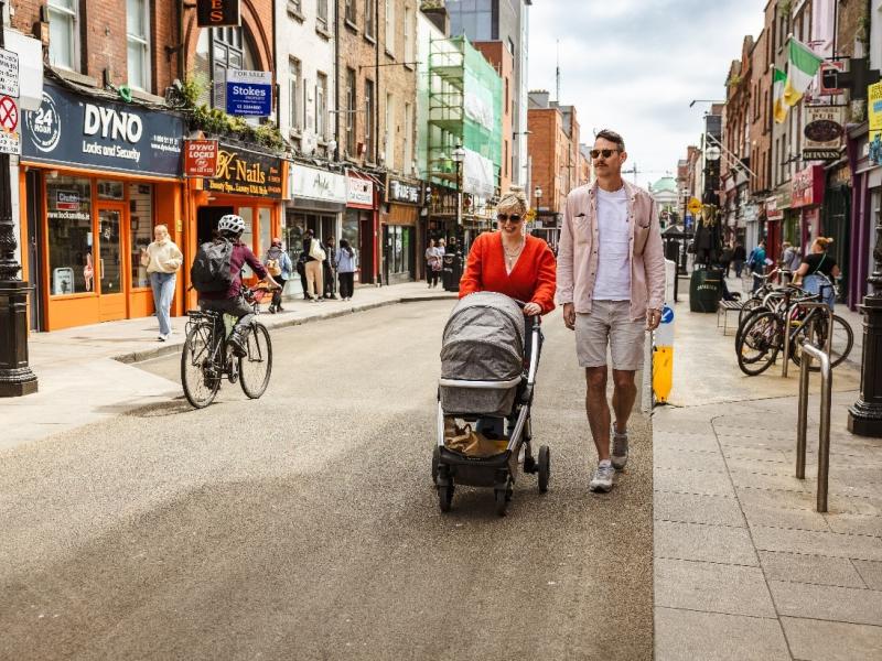 woman and man walking on pedestrian street, pushing a child in a pram