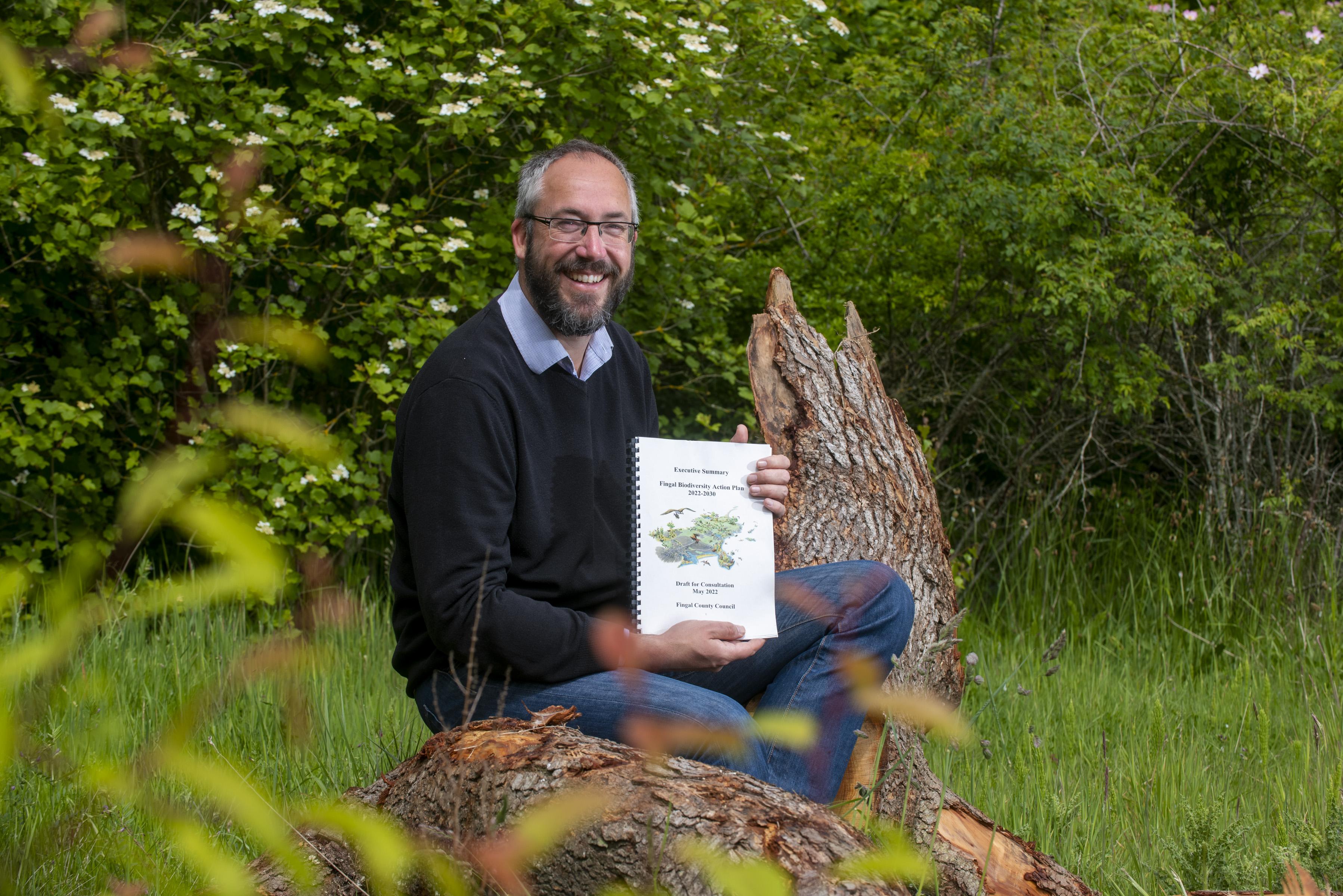 bearded man holding document while sitting on log in flowers and grass