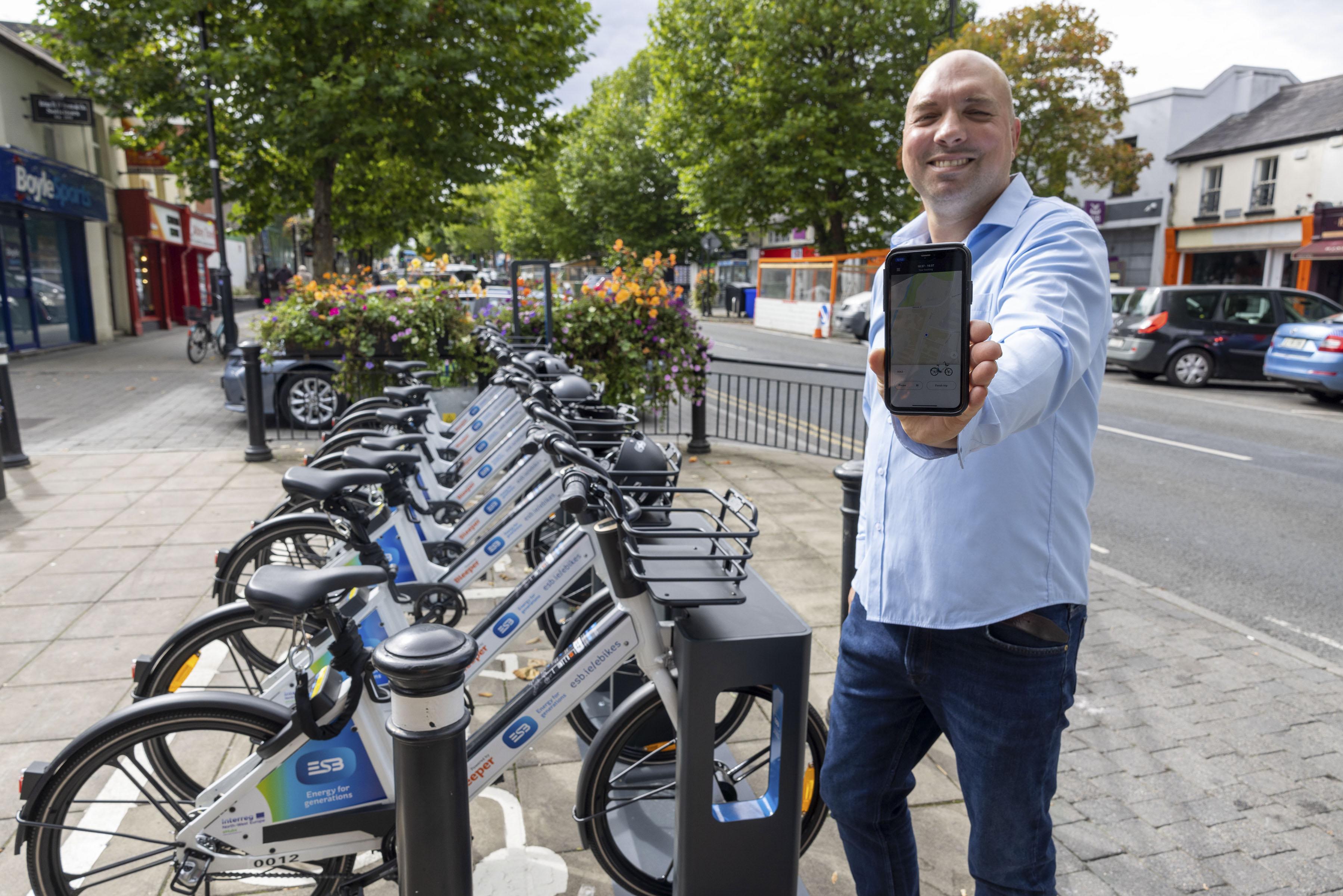 Man holding phone app up next to eBikes rack