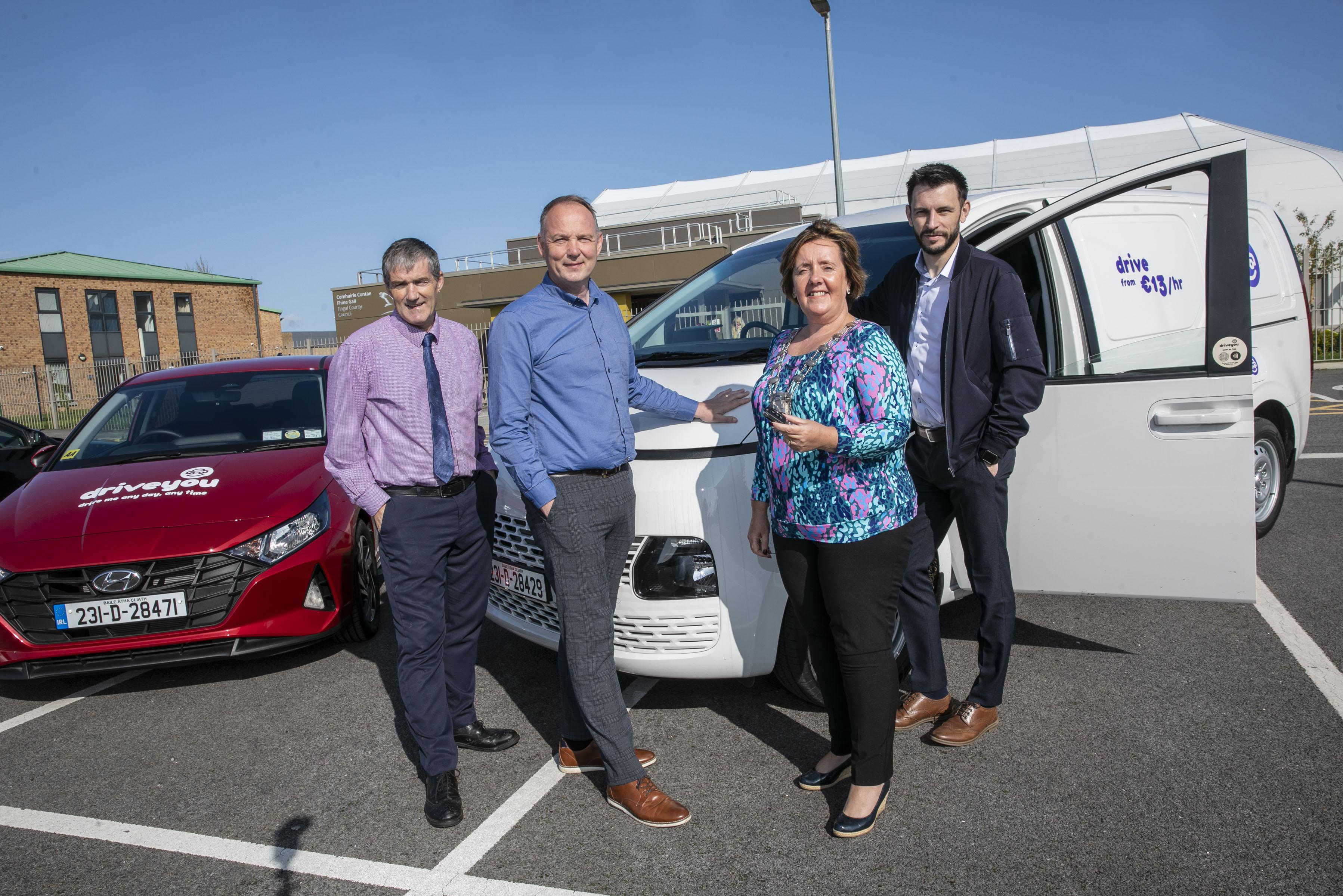 Woman holding keys stands next to vehicle surrounded by other people 
