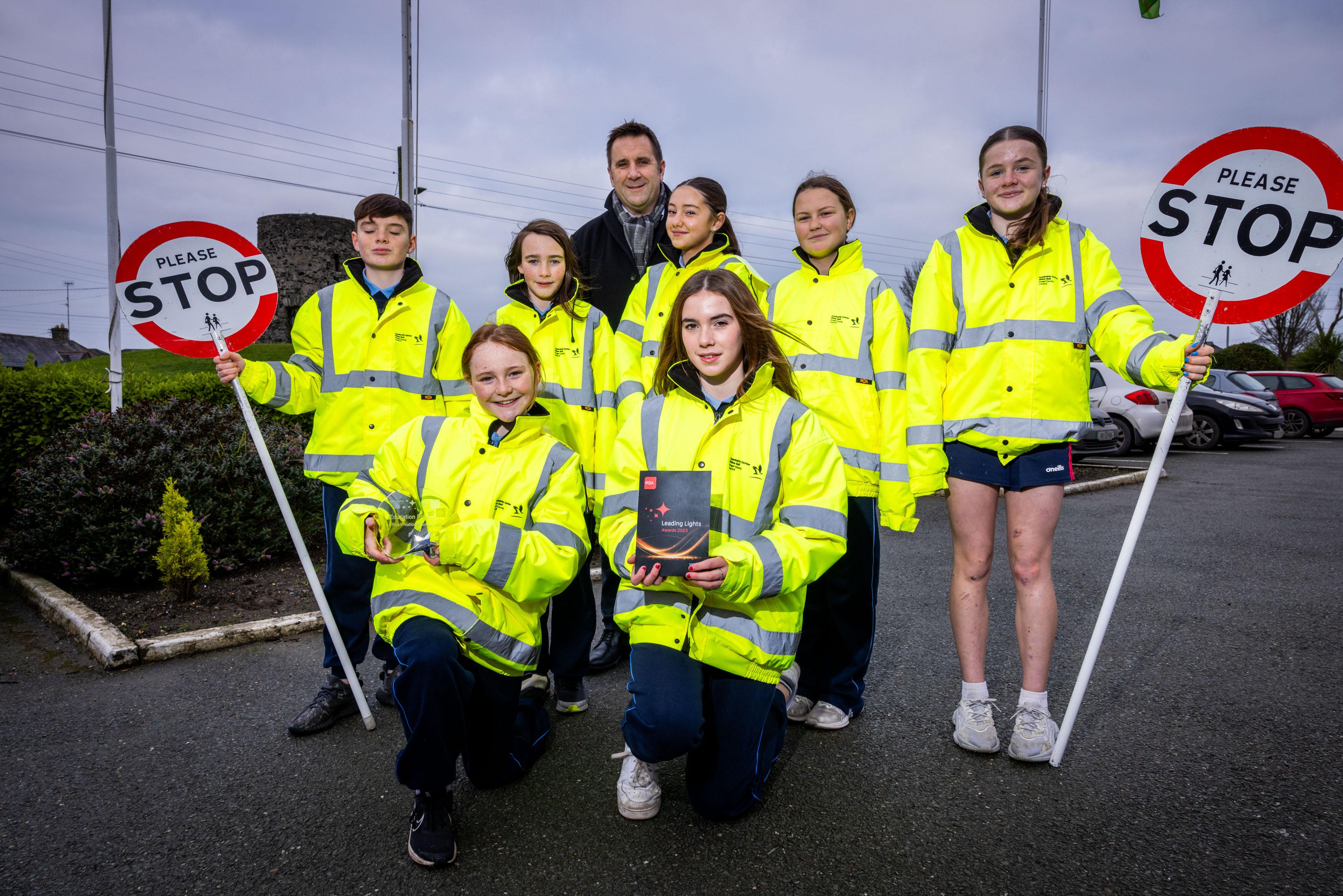 Group of children in yellow hi-vis jackets pose with school principal while holding award